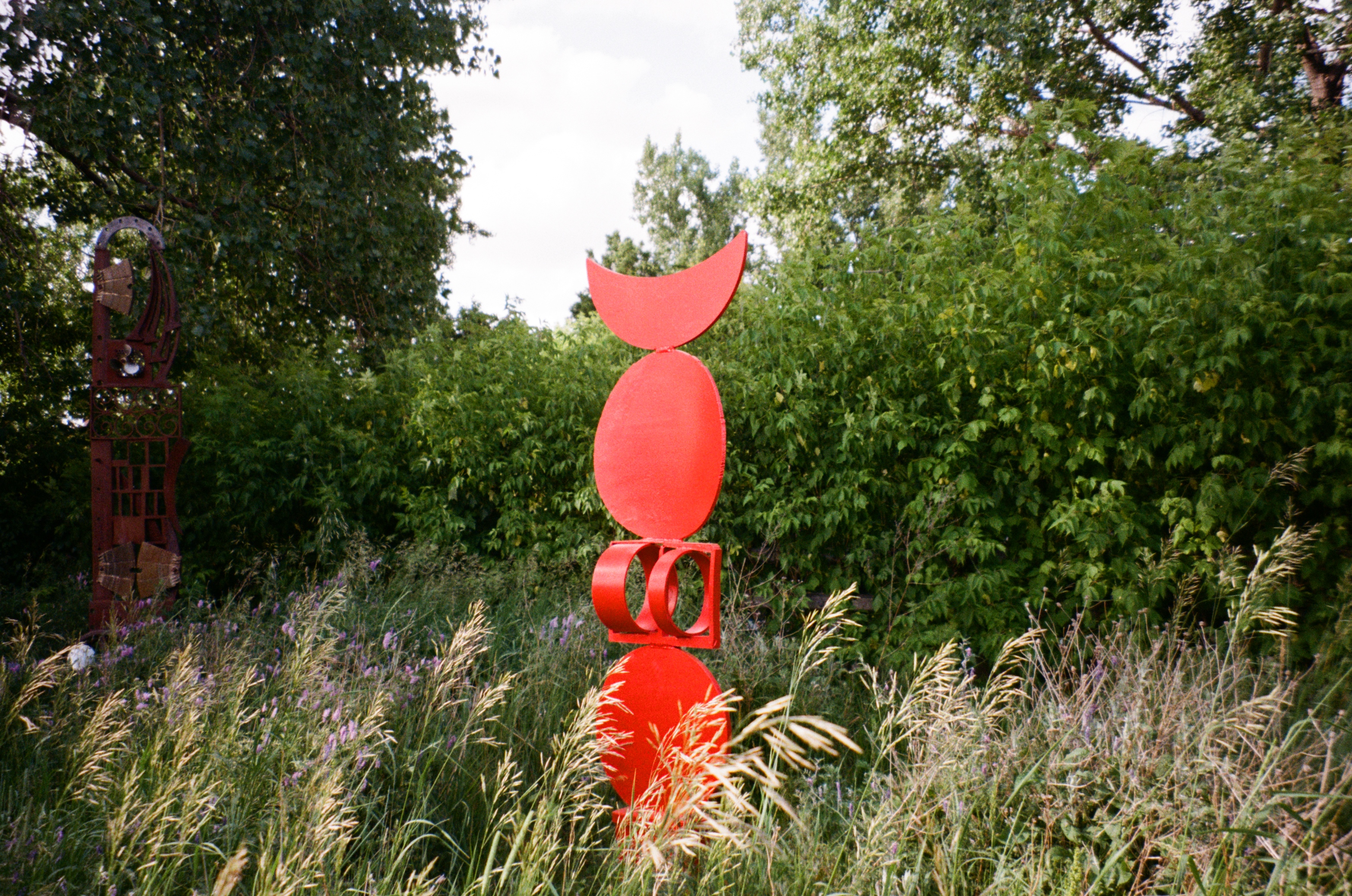 (film) Red sculpture in a field, surrounded by trees and other greenery